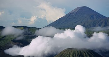 Movie still from “Into the Inferno” (2016), directed by Werner Herzog – A mountain range with a cloud filled sky above it; Extreme Wide shot, Low angle