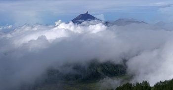 Movie still from “Into the Inferno” (2016), directed by Werner Herzog – A view of a mountain with clouds in the sky; Extreme Wide shot, High angle