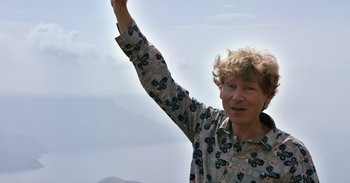 Movie still from “Into the Inferno” (2016), directed by Werner Herzog – An older woman raises her hand in the air; Medium shot, Overhead angle