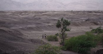 Movie still from “Into the Inferno” (2016), directed by Werner Herzog – A couple of people standing on top of a dirt field; Extreme Wide shot, High angle