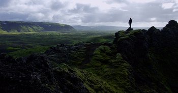 Movie still from “Into the Inferno” (2016), directed by Werner Herzog – A person standing on a cliff looking out over a valley; Extreme Wide shot, High angle