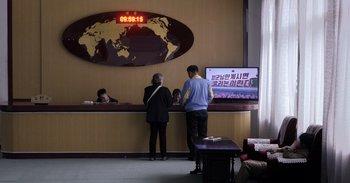 Movie still from “Into the Inferno” (2016), directed by Werner Herzog – Two people standing in front of a hotel lobby; Wide shot, High angle