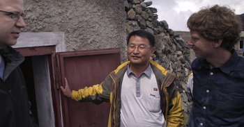 Movie still from “Into the Inferno” (2016), directed by Werner Herzog – A man standing in front of a stone wall; Medium shot, Low angle