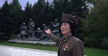Movie still from “Into the Inferno” (2016), directed by Werner Herzog – A woman in a military uniform points to a statue; Medium shot, Low angle