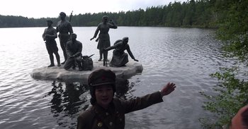 Movie still from “Into the Inferno” (2016), directed by Werner Herzog – A woman in a military uniform standing in a body of water near statues; Wide shot, High angle
