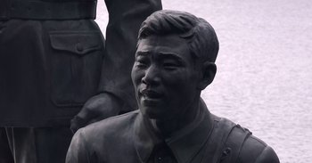 Movie still from “Into the Inferno” (2016), directed by Werner Herzog – A statue of a man in a suit; Close Up shot, High angle