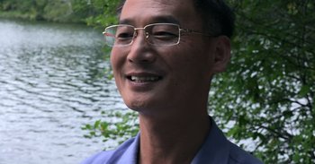 Movie still from “Into the Inferno” (2016), directed by Werner Herzog – A person wearing glasses near a body of water; Close Up shot, Low angle