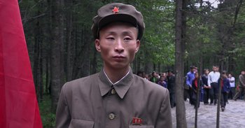 Movie still from “Into the Inferno” (2016), directed by Werner Herzog – A man in a military uniform with a red star on his hat; Close Up shot, Over the shoulder angle