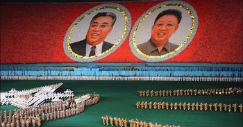 Movie still from “Into the Inferno” (2016), directed by Werner Herzog – A group of people standing in front of a wall with a picture on it; Extreme Wide shot, High angle