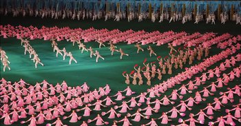 Movie still from “Into the Inferno” (2016), directed by Werner Herzog – A large group of people in pink outfits dancing; Extreme Wide shot, High angle
