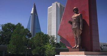 Movie still from “Into the Inferno” (2016), directed by Werner Herzog – A statue of a soldier in front of a large building; Wide shot, Low angle