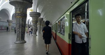 Movie still from “Into the Inferno” (2016), directed by Werner Herzog – A woman in a black dress walking on a train platform; Wide shot, Low angle