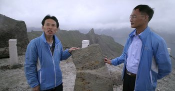Movie still from “Into the Inferno” (2016), directed by Werner Herzog – Two men standing next to each other on top of a mountain; Medium shot, Over the shoulder angle
