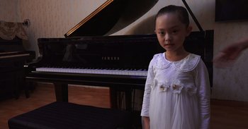 Movie still from “Into the Inferno” (2016), directed by Werner Herzog – A little girl standing in front of a piano; Close Up shot, High angle