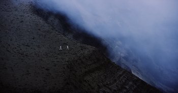 Movie still from “Into the Inferno” (2016), directed by Werner Herzog – A couple of people walking up a mountain side; Extreme Wide shot, High angle