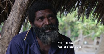 Movie still from “Into the Inferno” (2016), directed by Werner Herzog – An older man with a beard and a mustache; Medium shot, Over the shoulder angle