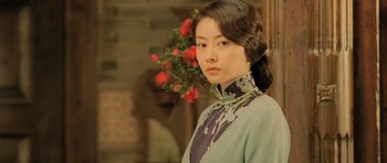 Movie still from “Ip Man” (2008), directed by Wilson Yip – A young woman in a dress standing in front of flowers; Medium shot, Low angle