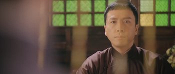 Movie still from “Ip Man” (2008), directed by Wilson Yip – A man in a brown shirt is sitting in front of a window; Close Up shot, Low angle