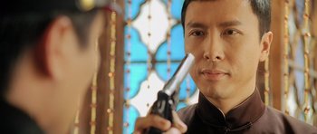 Movie still from “Ip Man” (2008), directed by Wilson Yip – A man holding a gun in front of a stained glass window; Close Up shot, Over the shoulder angle