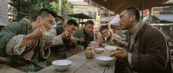 Movie still from “Ip Man” (2008), directed by Wilson Yip – A group of men sitting at a wooden table eating food; Medium shot, Low angle