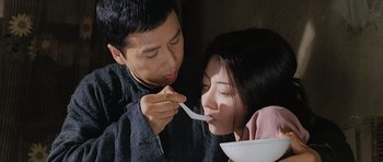 Movie still from “Ip Man” (2008), directed by Wilson Yip – A man feeding a spoon to a woman with a bowl; Medium shot, Low angle