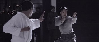 Movie still from “Ip Man” (2008), directed by Wilson Yip – A man in a grey shirt is practicing martial arts; Medium shot, Over the shoulder angle