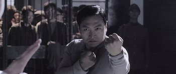 Movie still from “Ip Man” (2008), directed by Wilson Yip – A man in a gray jacket is holding his fist up; Medium shot, Low angle