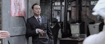 Movie still from “Ip Man” (2008), directed by Wilson Yip – A man wearing a suit and tie holding a book; Medium shot, Low angle