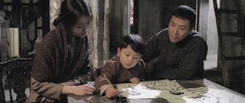 Movie still from “Ip Man” (2008), directed by Wilson Yip – A young boy sitting at a table with two adults; Medium shot, High angle