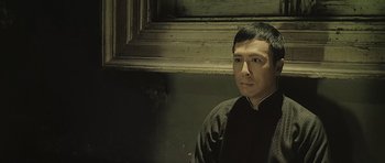 Movie still from “Ip Man” (2008), directed by Wilson Yip – A man sitting in front of a window in a dark room; Close Up shot, Low angle
