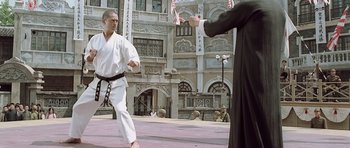 Movie still from “Ip Man” (2008), directed by Wilson Yip – A man in a black robe and a man in a white shirt and black pants are practicing martial arts in front of a building; Wide shot, Low angle