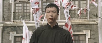 Movie still from “Ip Man” (2008), directed by Wilson Yip – A man standing in front of a bunch of flags; Close Up shot, Low angle