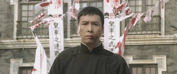 Movie still from “Ip Man” (2008), directed by Wilson Yip – A man wearing a black jacket standing in front of a building; Close Up shot, Low angle
