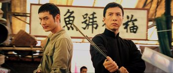 Movie still from “Ip Man 2” (2010), directed by Wilson Yip – A man holding a pair of chopsticks while standing next to another man; Close Up shot, Low angle