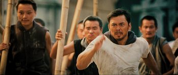 Movie still from “Ip Man 2” (2010), directed by Wilson Yip – A group of men standing next to each other holding wooden poles; Medium shot, Over the shoulder angle