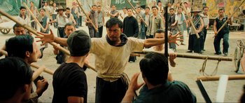 Movie still from “Ip Man 2” (2010), directed by Wilson Yip – A group of men standing in front of a man holding a sword; Medium shot, Over the shoulder angle