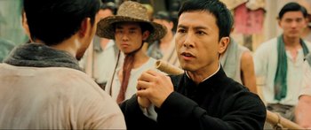 Movie still from “Ip Man 2” (2010), directed by Wilson Yip – A man holding a wooden stick in front of a crowd; Close Up shot, Over the shoulder angle