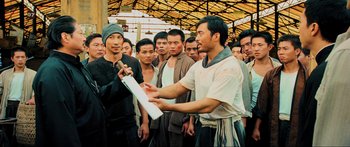 Movie still from “Ip Man 2” (2010), directed by Wilson Yip – A group of men standing around a building; Medium shot, Over the shoulder angle