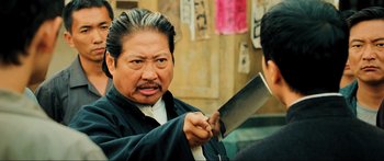 Movie still from “Ip Man 2” (2010), directed by Wilson Yip – A man holding a knife in front of a wall; Close Up shot, Over the shoulder angle