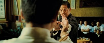 Movie still from “Ip Man 2” (2010), directed by Wilson Yip – A man in a black suit and white shirt clapping hands; Medium shot, Over the shoulder angle