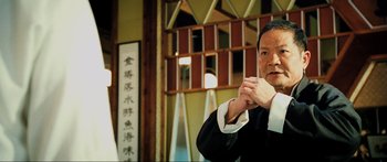 Movie still from “Ip Man 2” (2010), directed by Wilson Yip – A man in a black suit is holding his hands up; Close Up shot, Low angle