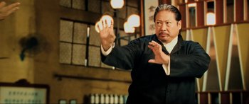 Movie still from “Ip Man 2” (2010), directed by Wilson Yip – A man in a suit and tie holding his hands up; Medium shot, Low angle