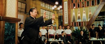 Movie still from “Ip Man 2” (2010), directed by Wilson Yip – A man in a black suit is directing a group of people; Medium shot, Low angle