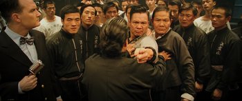 Movie still from “Ip Man 2” (2010), directed by Wilson Yip – A group of men standing around each other in a room; Medium shot, Over the shoulder angle