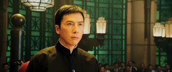 Movie still from “Ip Man 2” (2010), directed by Wilson Yip – A man in a black suit standing in front of a crowd of onlookers; Close Up shot, Low angle