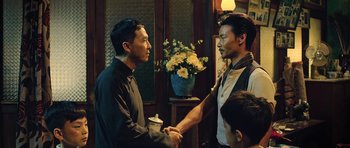 Movie still from “Ip Man 3” (2015), directed by Wilson Yip – Two asian men shaking hands in front of a vase of flowers; Medium shot, Over the shoulder angle