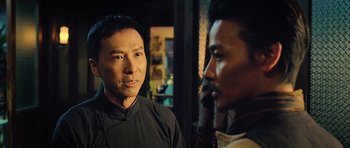Movie still from “Ip Man 3” (2015), directed by Wilson Yip – A man standing next to another man in front of a window; Close Up shot, Over the shoulder angle
