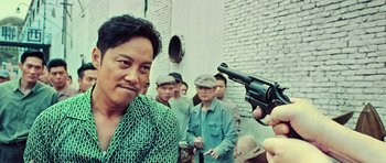 Movie still from “Ip Man 3” (2015), directed by Wilson Yip – A group of people standing around a man holding a gun; Close Up shot, Over the shoulder angle