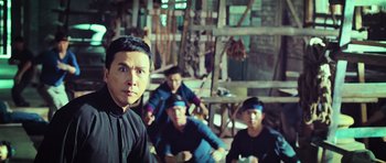 Movie still from “Ip Man 3” (2015), directed by Wilson Yip – A group of men sitting on the ground in front of a wooden structure; Medium shot, Over the shoulder angle