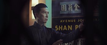 Movie still from “Ip Man 3” (2015), directed by Wilson Yip – A man in a black shirt is standing in front of a sign; Medium shot, Low angle